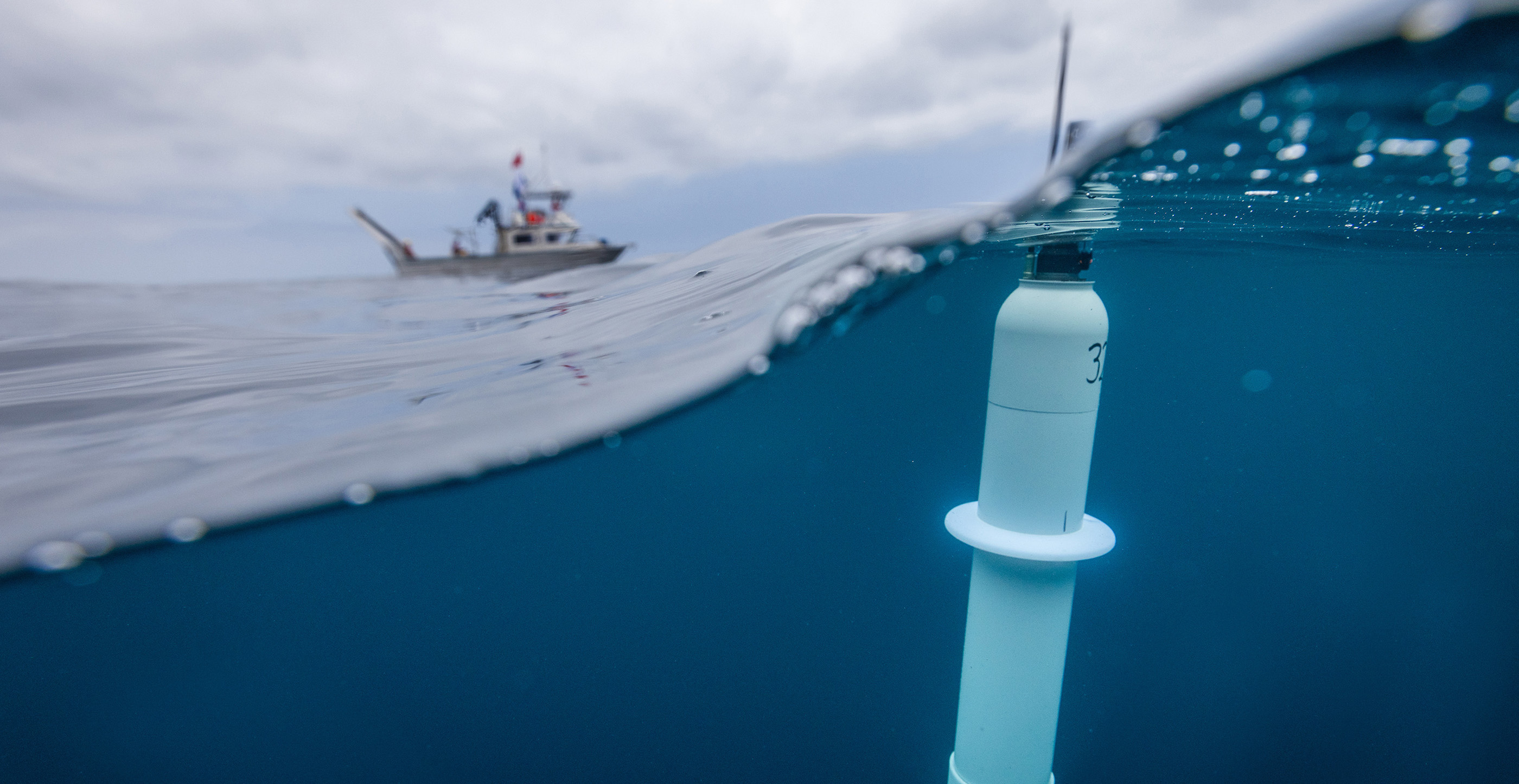 Data collection tool floats in ocean with research vessel in distance